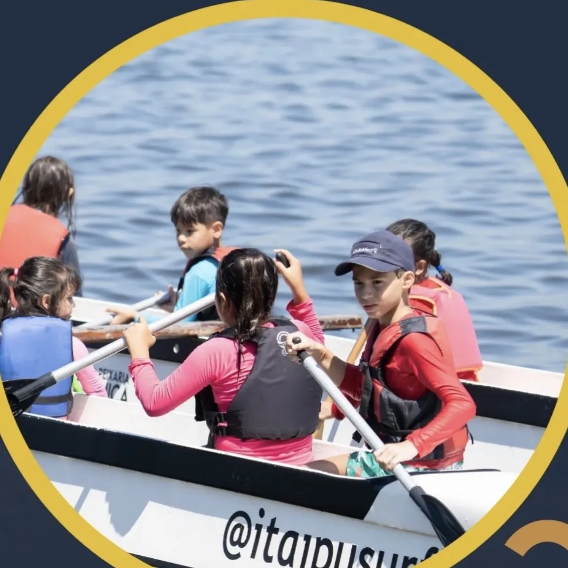 Crianças de colete salva-vidas remando lado a lado dentro da canoa polinésia, cada uma olhando para uma direção diferente.