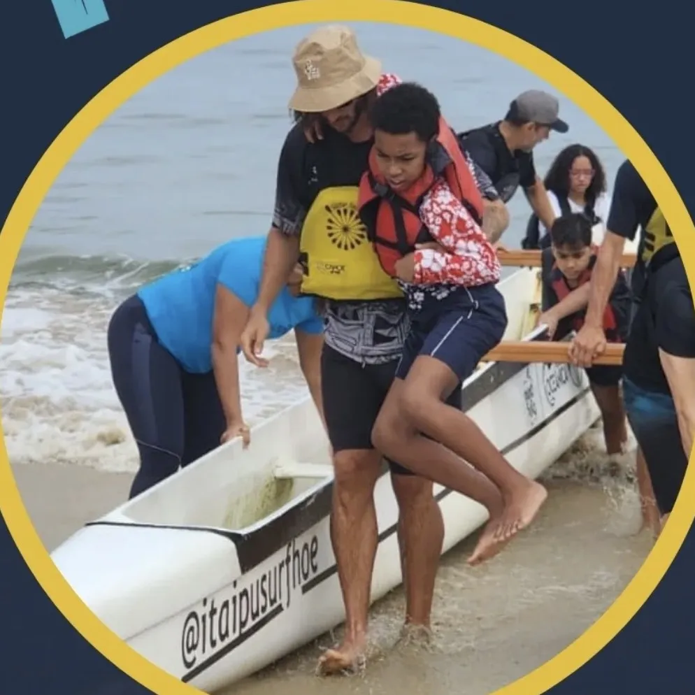 Facilitador apoia um adolescente de colete salva-vidas na saída da canoa, enquanto outra pessoa da equipe segura a embarcação.