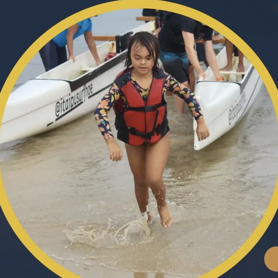 Menina com síndrome de Down sai da água de colete salva-vidas depois da remada, ao lado da canoa polinésia.
