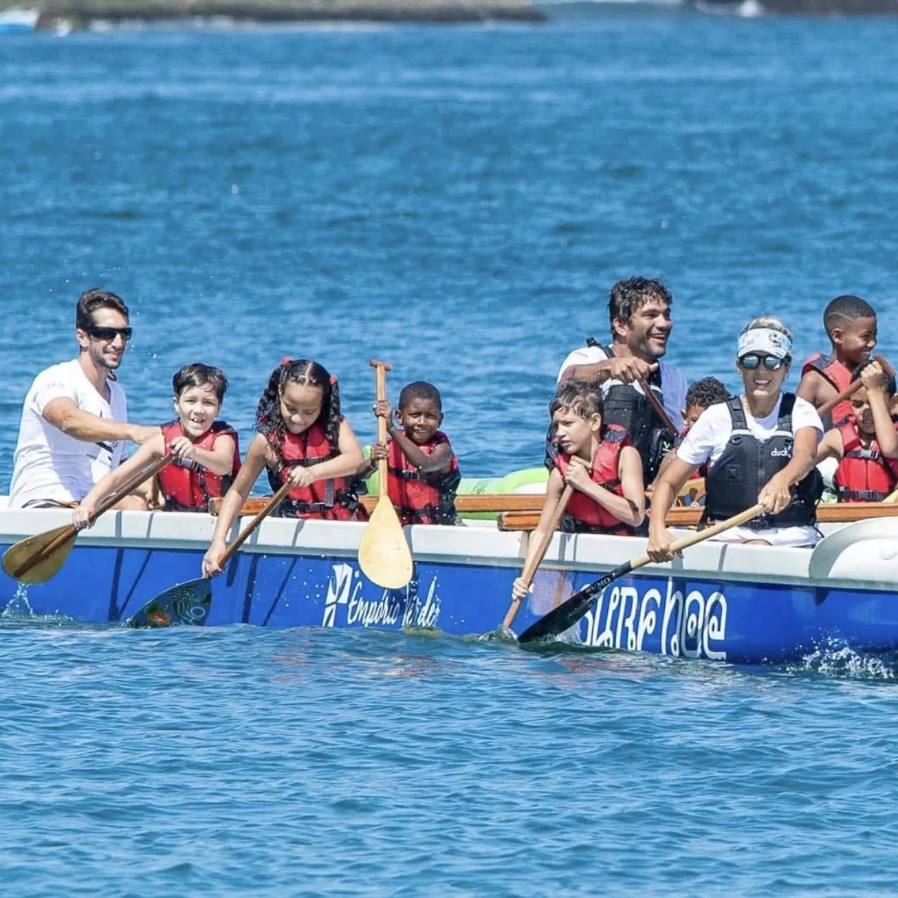 Canoa polinésia cheia, com crianças e facilitadores remando em sincronia no mar de Niterói.