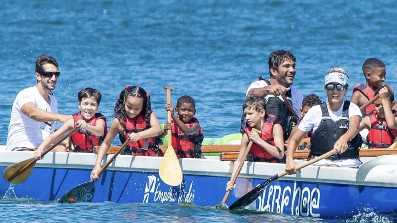 Canoa polinésia cheia, com crianças e facilitadores remando em sincronia no mar de Niterói.